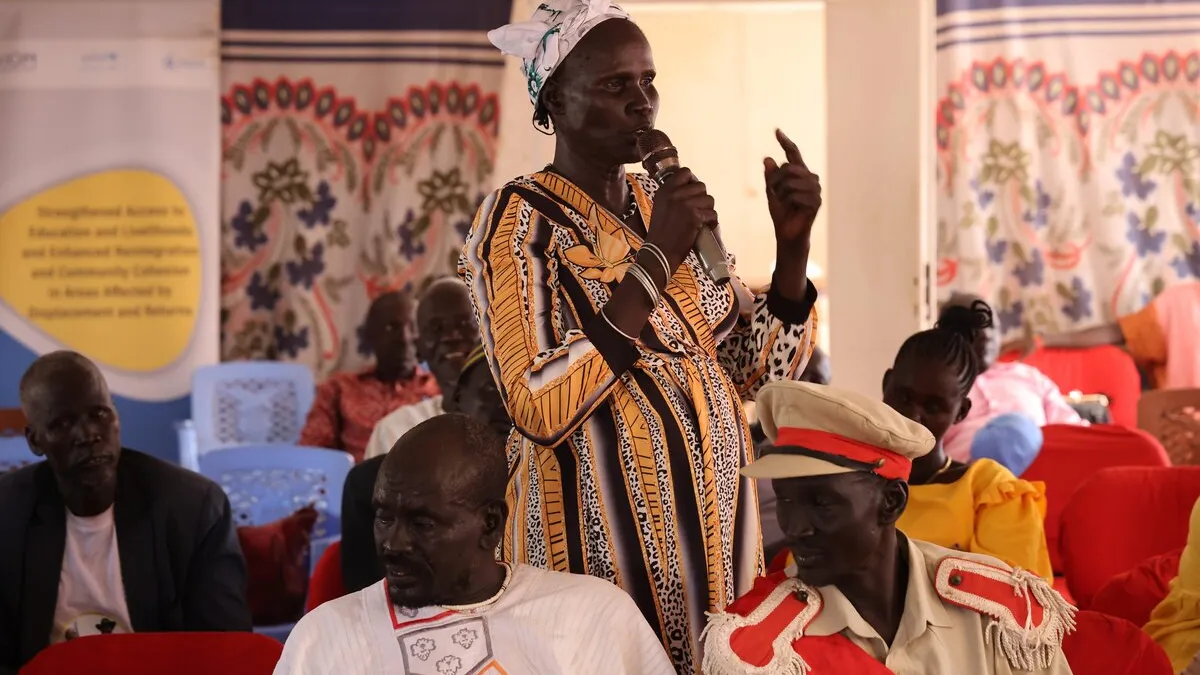 In Kuajok, a harmonization workshop on customary law in Warrap State led to the consensual abolishment of early and forced marriage. Pending on state government approval, this decision will soon be translated into formal law. Person speaking into a microphone while standing among seated participants in a hall decorated with patterned fabric and banners.