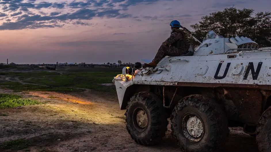 Un casque bleu de l'ONU assis sur un véhicule, les yeux rivés sur le coucher de soleil.