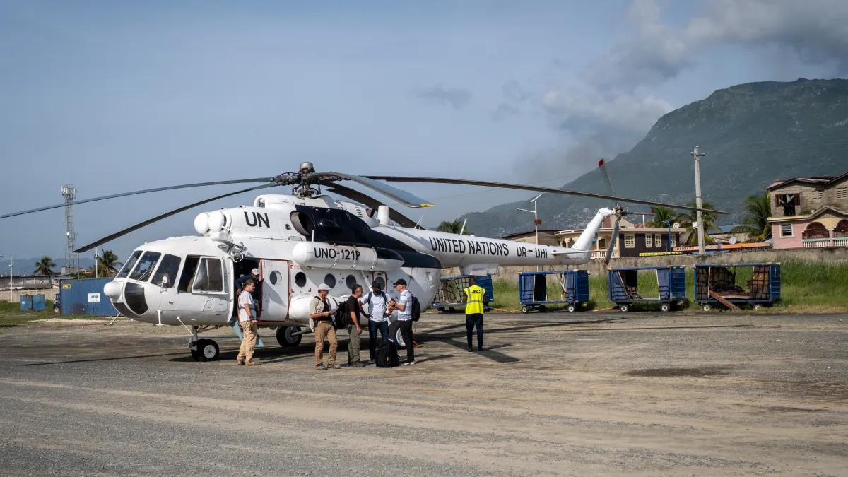 A United Nations helicopter on the ground in Cap-Haïtien, Haiti, with personnel gathered beside the aircraft