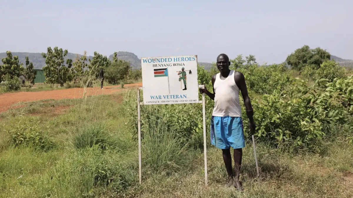 A member of the Wounded Heroes farming group stands beside the group’s sign in Bilinyang Payam, Central Equatoria State. The group consists of internally displaced, conflict-injured former soldiers who now farm on land cleared by UNMAS