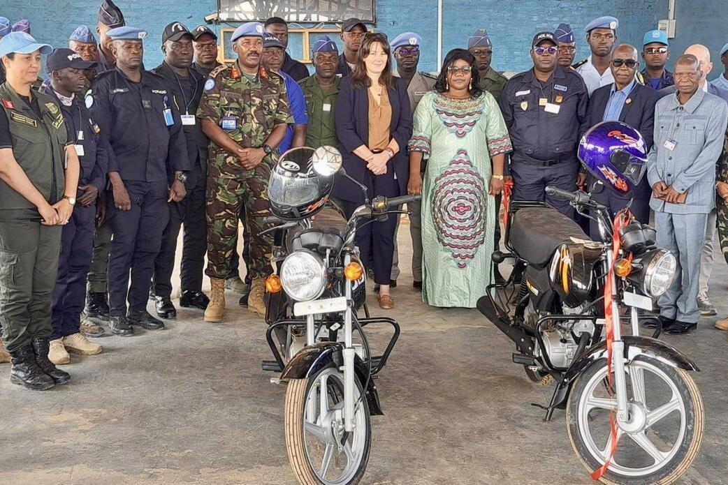 Un groupe de militaires et de civils servant la paix se tient derrière deux motos.