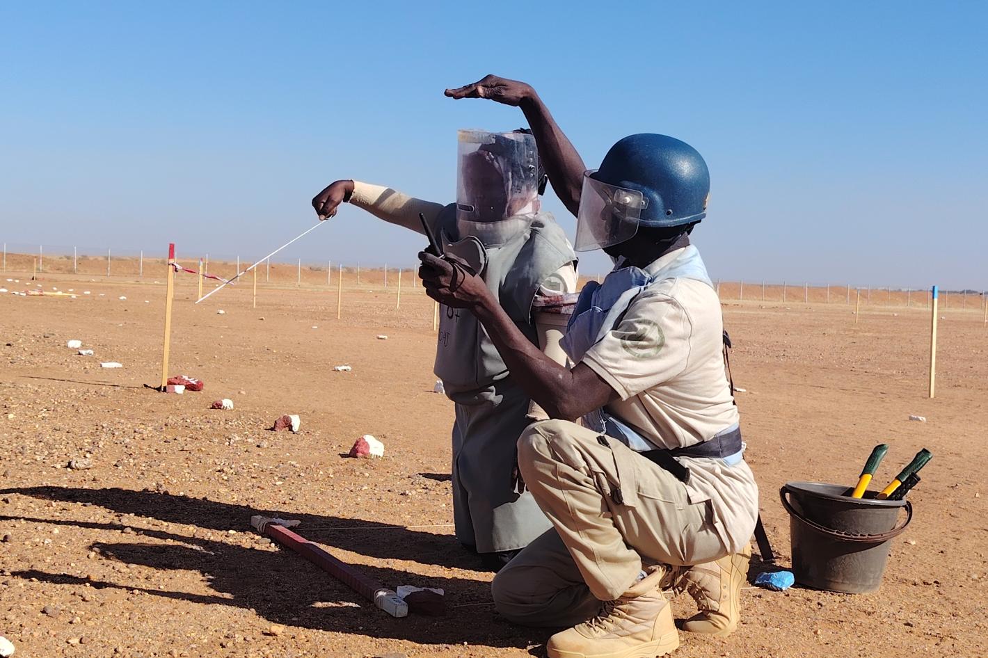 a deminer is receiving training from another deminer in the field