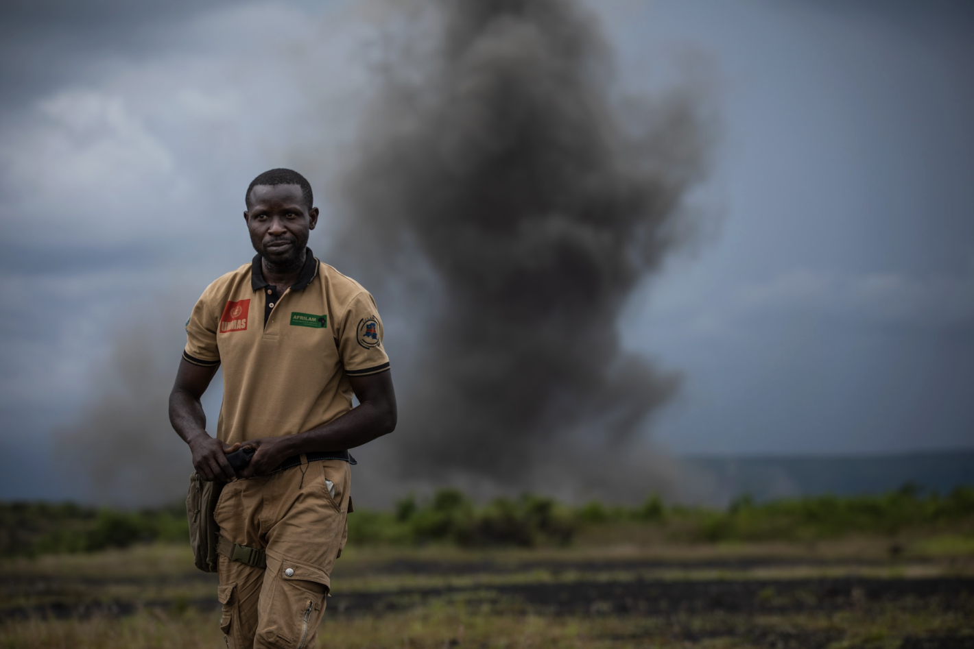 a man is standing in a field with smoke behind him.