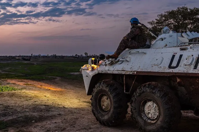 Un casque bleu de l'ONU assis sur un véhicule, les yeux rivés sur le coucher de soleil.