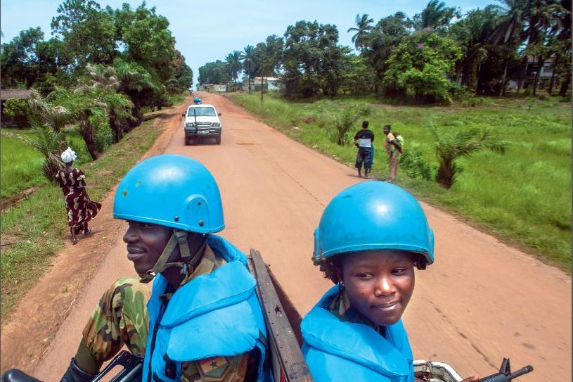 Peacekeepers sit on the back of a truck, travelling down a dirt road