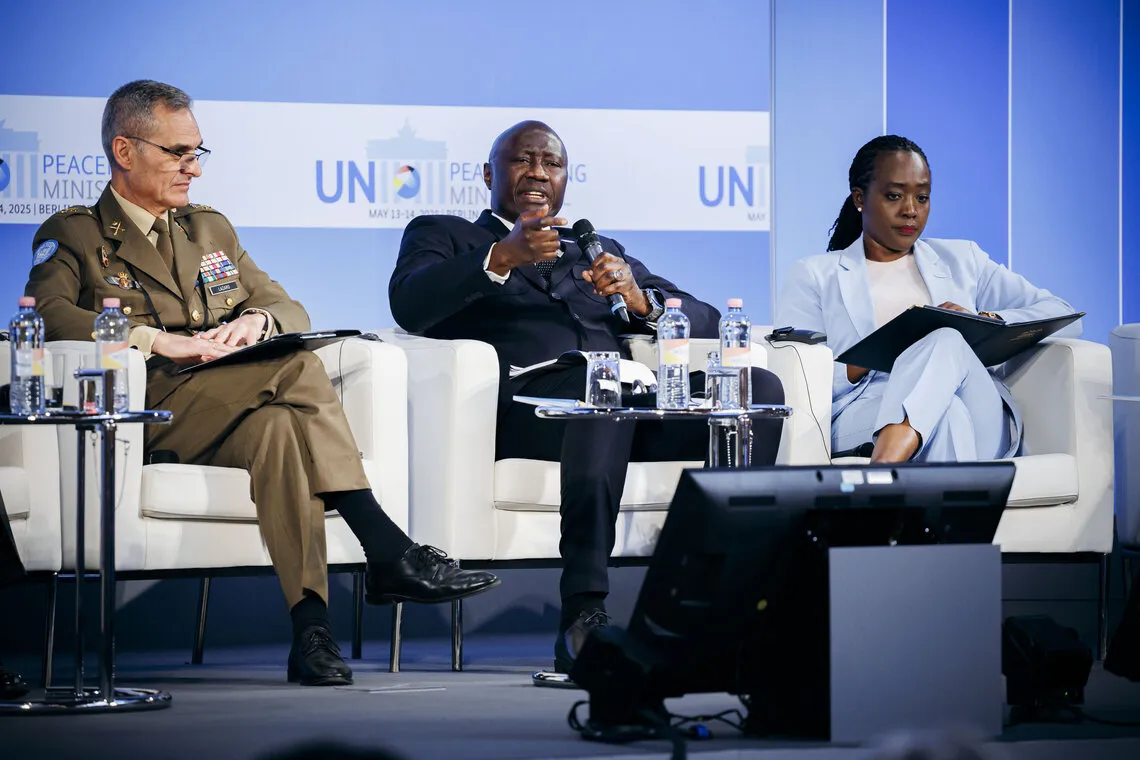 A man addressing the audience seated with two other members of a panel.