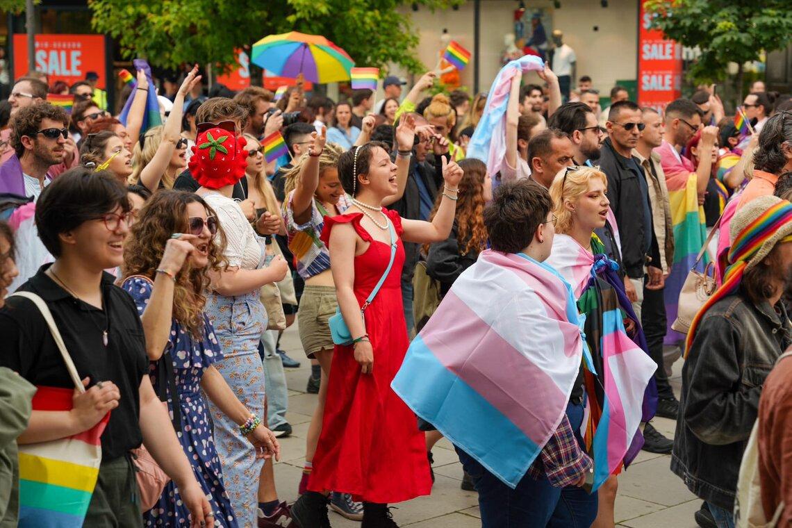 People march in a pride parade, draped in colourful flags